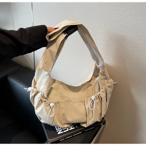 Close-up of cream pleated tote bag featuring drawstring side pockets and wide strap