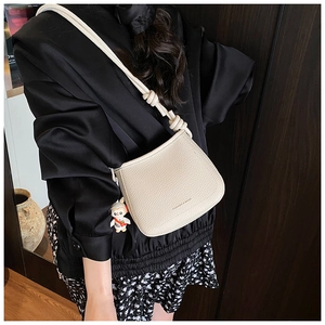Detail of beige grainy leather bucket bag with knotted rope strap and rabbit charm