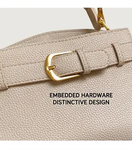 Détail du cuir grainé litchi et boucle dorée sur un sac à main élégant de couleur crème