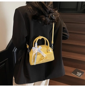 Detail of yellow semi-circle crossbody bag with blue plaid bow on wood stairs