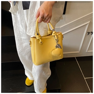 Detail of yellow bucket bag with knotted handle, litchi texture and heart pendant