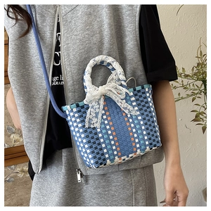 Detail of blue woven handbag featuring white lace bow handle and colorful pattern