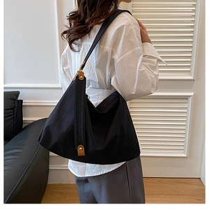 Detail of a large black pleated tote bag with leather straps and gold buckles on a model
