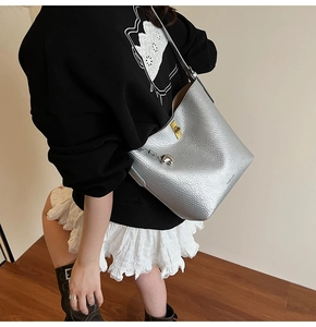 Detail of silver lychee grain leather bucket bag featuring a gold metal lock and heart charm