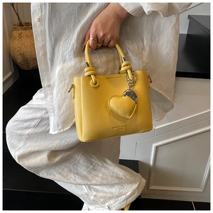Detailed macro shot of yellow litchi pattern leather bucket bag with heart pendant charm