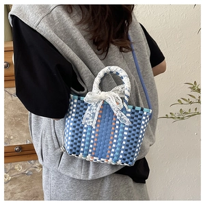 Detail of multi-color woven handbag with lace bow and blue crossbody strap on a model
