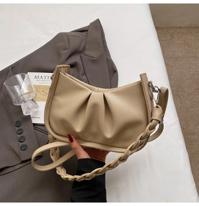 Detailed view of beige pleated handbag with woven strap next to a grey blazer