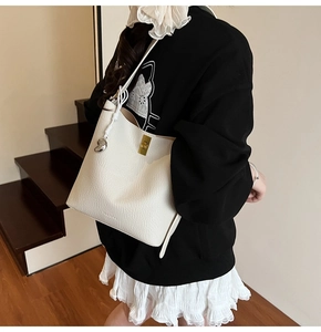 Close-up of a white lychee grain bucket bag featuring a gold lock and heart pendant
