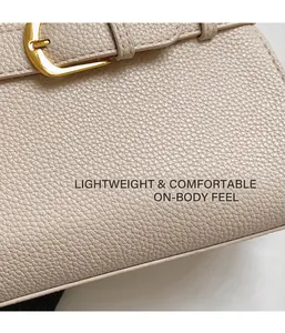 Gros plan sur la texture du cuir litchi et la boucle en métal doré d'un sac à main beige