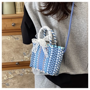 Blue and white woven mini crossbody bag with lace bow detail shown on a female model