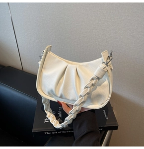 Detail of white pleated crescent bag with textured leather and woven shoulder strap