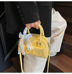 Detail of yellow leather Boston bag with decorative bow and plaid lace ribbon handle