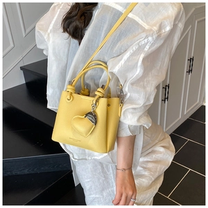 Detailed view of yellow lychee grain leather bucket bag with heart-shaped charm on a model