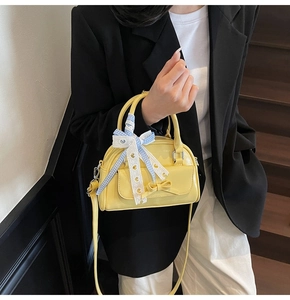 Detail of a bright yellow patent leather handbag featuring a stylish decorative bow tie