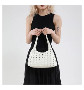 Close-up of white leather underarm bag with decorative metal eyelets and modern industrial style
