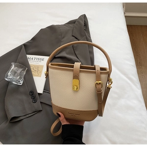 Détail d'un sac seau bicolore en cuir grainé crème avec des accents dorés