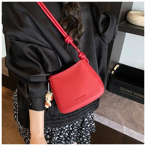 Detail of red pebbled leather bucket bag with knotted strap and cartoon charm accessory