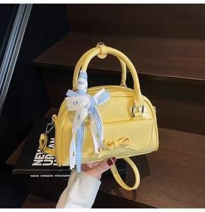 Detail of yellow mini Boston bag with ribbon bow and lace strap on wooden steps