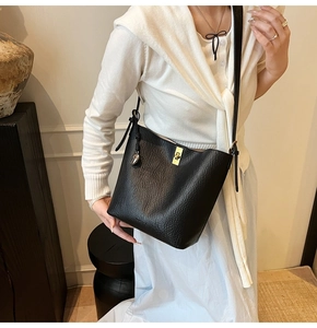 Detailed view of black lychee leather bucket bag featuring a gold clasp and side tassels