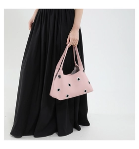 Pink rivet hollowed-out shoulder bag with silver eyelets shown against black pleated dress