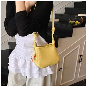 Detailed shot of yellow bucket bag featuring a knot strap and cute doll pendant