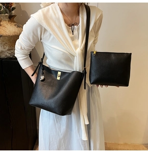 Detail of black pebbled leather bucket bag set with gold lock and metal charm pendant