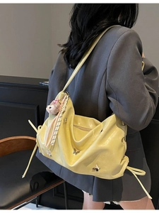 Fashionable yellow pleated shoulder bag with metallic butterfly accents and plush charm