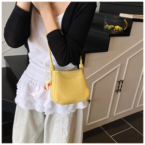 Close-up of a yellow pebbled leather bucket bag with rope knot strap and bunny charm