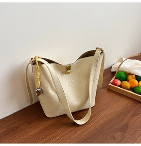 Detail of cream hobo bag with pebble leather, gold twist lock and woven charm on a desk