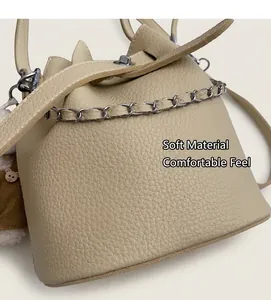 Close-up of beige bucket bag with lychee grain leather, silver chain and bear charm