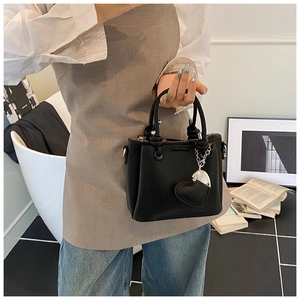 Detail of black lychee grain leather bucket bag featuring a heart-shaped charm and round handles