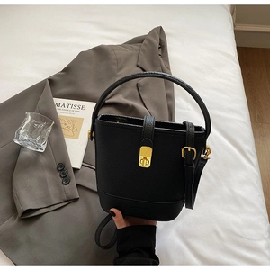 Détail du sac seau noir en cuir litchi avec fermoir en métal doré sur veste grise