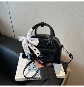 Detail of glossy black shell handbag featuring decorative bow and blue plaid ribbon accent