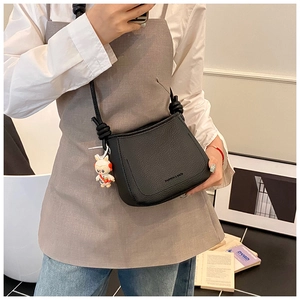 Detail of black lychee grain shoulder bag with knot strap and white rabbit pendant