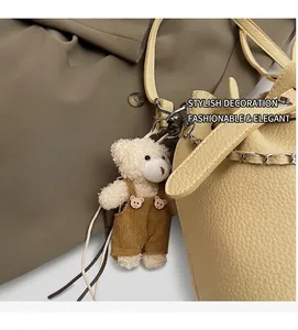 Close-up of beige litchi grain leather bucket bag with a cute plush bear charm accessory