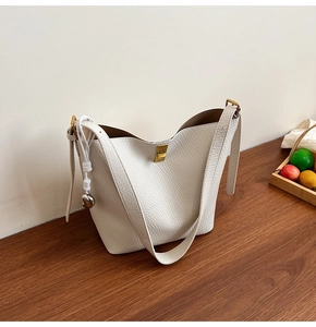 Close-up of white lychee leather bucket bag with gold clasp and woven pendant detail