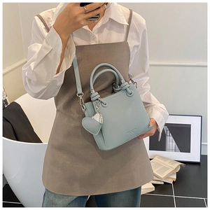 Detail of light blue bucket bag with lychee grain leather, round handles and heart charm