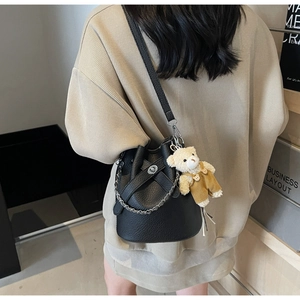 Detail of black lychee grain leather bucket bag with silver chain and cute bear charm