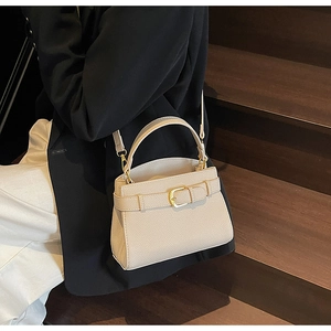 Détail d'un sac bandoulière crème avec boucles dorées porté par une femme en tailleur