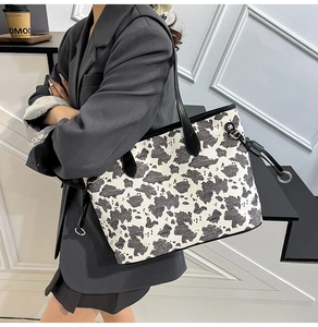 Vista a spalla della borsa tote grande in tela con stampa mucca e manici in pelle
