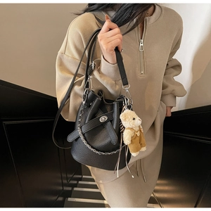 Detail of black pebbled leather bucket bag with chain strap and teddy bear charm
