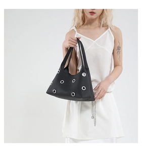 Detail of black trapezoid tote bag with silver metal eyelets on textured leather