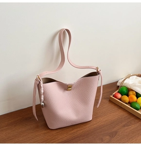 Detail of light pink pebble leather bucket bag featuring gold metal turn-lock and ball charm
