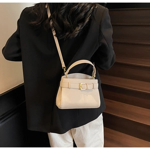 Sac bandoulière beige en cuir porté par un mannequin avec costume noir et pantalon blanc
