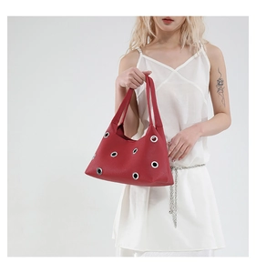 Detail of red pebbled leather shoulder bag with decorative silver grommets and thin handle