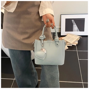 Detail of mint green bucket bag featuring pebbled leather and heart chain charm