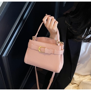 Détail d'un sac à main en cuir rose avec boucle dorée porté par un mannequin en extérieur