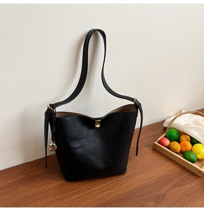 Detail of black pebbled leather bucket bag with gold clasp and heart pendant on wood table