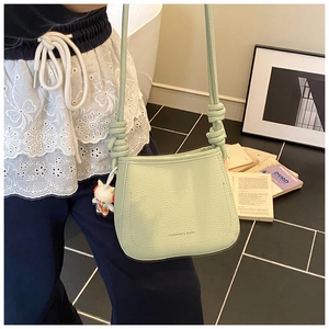 Detail of mint green bucket bag featuring pebbled texture and rope knot shoulder strap