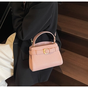 Vue détaillée du sac à main rose en cuir grainé avec boucle dorée sur des marches